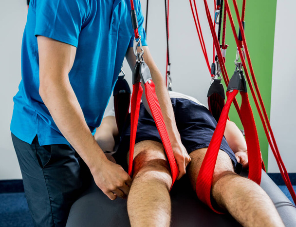 Physiotherapy. Suspension training therapy. Young man doing fitness traction therapy with suspension-based exercise training system. Treatment of pain in the spine. - 写真・画像