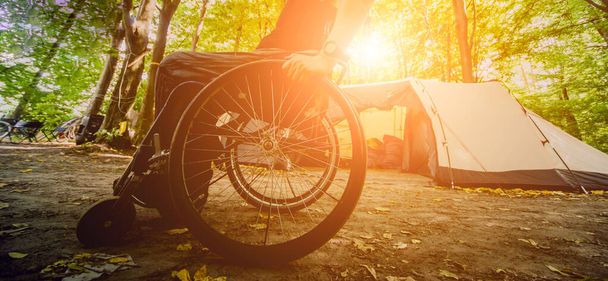 Behinderter Mann, der mit Freunden auf einem Campingplatz ruht. Rollstuhl im Wald auf dem Hintergrund der Zelte. Zelten. Sommerzeit - Foto, Bild