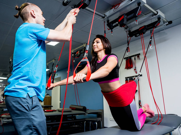 Young woman doing fitness traction therapy with suspension-based exercise training system. Physiotherapy concept - Fotografie, Obrázek