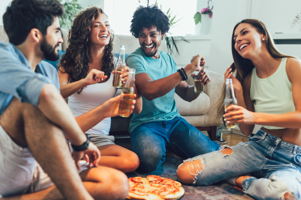 Ryhmä monikansallisia nuoria ystäviä syö pizzaa kotona ja hav
 - Valokuva, kuva