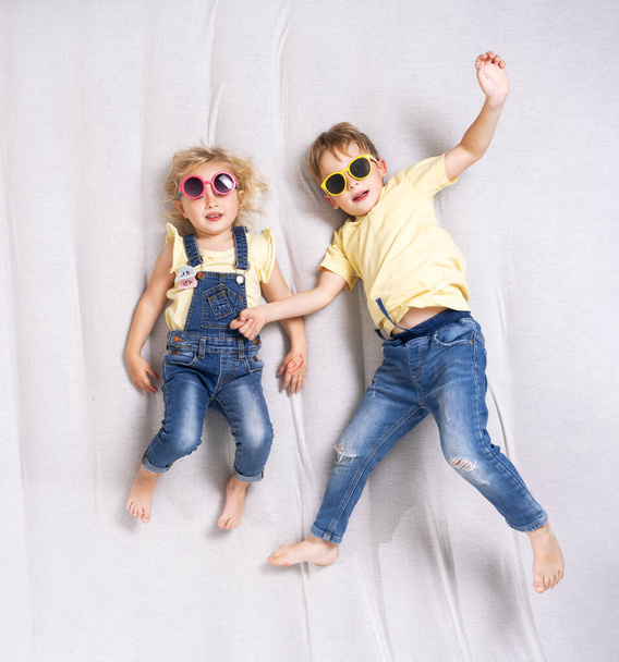 Little boy and girl in sunglasses lie on the sofa and have fun. - Foto, imagen