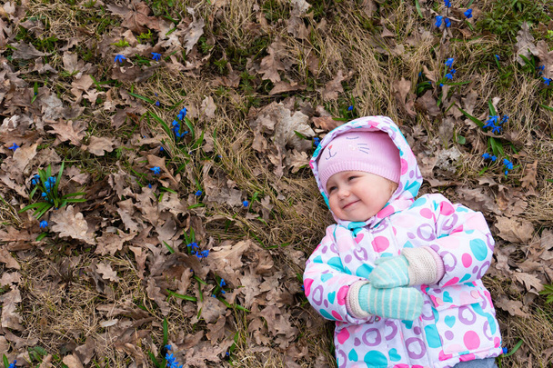 Little smiling girl lying down in the field of snowdrop flowers - Photo, Image