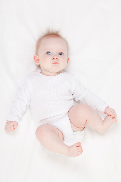 Cute baby with beautiful blue eyes lying in white bed - Fotoğraf, Görsel
