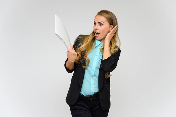 Portrait of a pretty blonde girl financial secretary with long curly hair in a business suit standing in the studio on a white background with emotions in different poses with a folder in his hands. - Photo, image