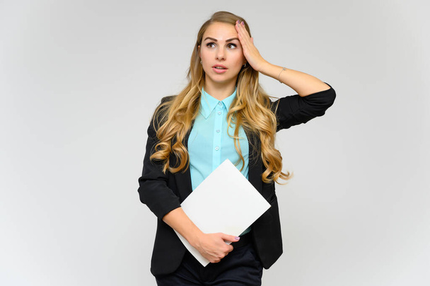 Portrait of a pretty blonde girl financial secretary with long curly hair in a business suit standing in the studio on a white background with emotions in different poses with a folder in his hands. - Foto, afbeelding