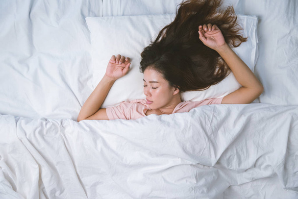 Teenager-Mädchen schläft ausgeruht. Gute Nachtruhe Konzept. Mädchen im Pyjama schläft morgens auf einem Bett in einem weißen Zimmer. warmer Ton. - Foto, Bild