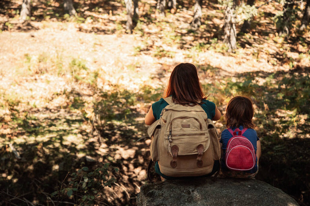 Anya és lánya együtt ülnek egy kövön az erdőben. - Fotó, kép