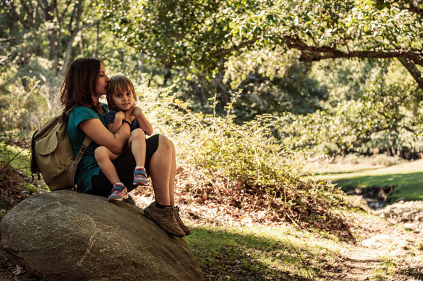 Μητέρα και κόρη κάθονται αγκαλιασμένοι σε μια πέτρα στο δάσος - Φωτογραφία, εικόνα
