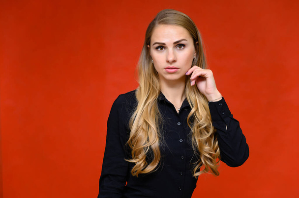 Πορτρέτο ενός όμορφου ξανθού κορίτσι οικονομική γραμματέας με μακριά σγουρά μαλλιά σε ένα κοστούμι επιχείρηση στέκεται στο στούντιο σε ένα κόκκινο φόντο με συναισθήματα σε διαφορετικές στάσεις. - Φωτογραφία, εικόνα
