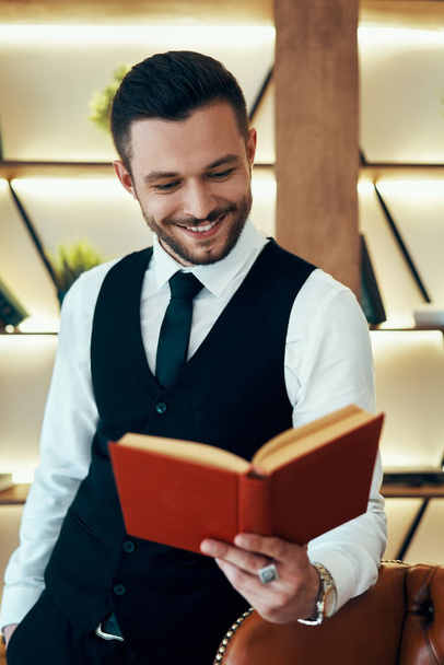 Handsome young man in elegant suit reading a book in modern luxury interior. Hobby concept - Photo, Image