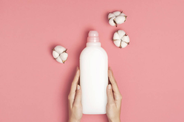 Ekopuhdistuskonsepti. Naisten kädet pitävät valkoista muovipakkausta pyykinpesuaineesta, nestemäisestä jauheesta, pesuaineesta, puuvillan kukista vaaleanpunaisella taustalla. Tasainen lay top näkymä. Bioorgaaninen tuote
 - Valokuva, kuva