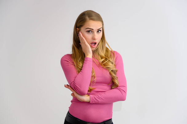 Close-up portrait of a pretty blonde girl with long curly hair standing in the studio on a white background with emotions in different poses in a pink sweater. Beauty, Model, Cosmetics - Foto, Imagen