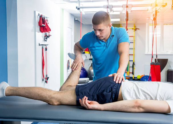 Rehabilitation therapy. Physiotherapist working with young male patient in the rehabilitation center. Treatment pain in spine - Фото, изображение