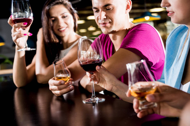 Vrolijke vrienden in de pub. Bier, wijn en whisky drinken, praten, plezier hebben. Vrienden ontmoeten na het werk - Foto, afbeelding