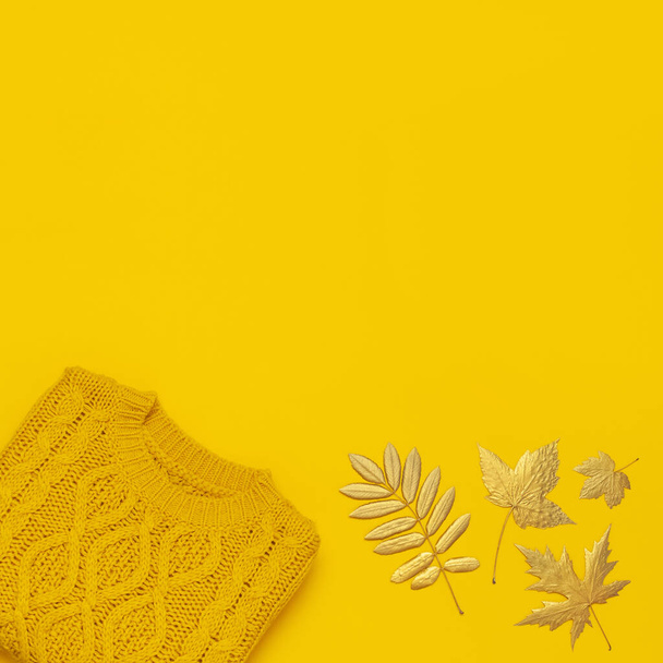 秋のフラットレイ構成。オレンジイエローのニットウールの女性のセーターと黄色の背景の上のビューに金色の葉。ファッショナブルな女性の秋のアクセサリー。居心地の良いニットジャンパースタイリッシュな女性の服 - 写真・画像