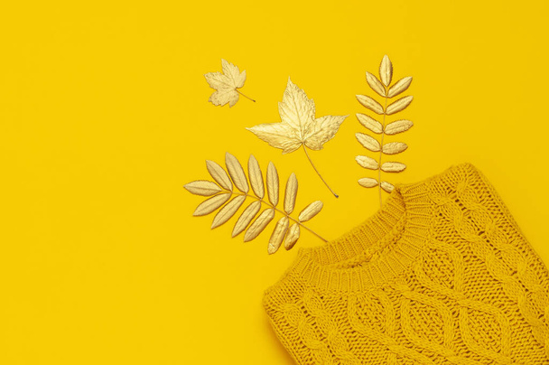 Осенняя плоская композиция. Оранжевый желтый вязаный шерстяной женский свитер и золотые листья на желтом фоне сверху. Модные женские осенние аксессуары. Уютная и стильная женская одежда
 - Фото, изображение