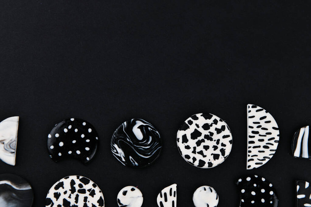 Um produto de argila polimérica. Argila de polímero preto e branco. Escultura à mão, produto para brincos em um fundo preto. Vista de cima. Brincos de jóias preto e branco. Jóias de argila de polímero artesanal
 - Foto, Imagem