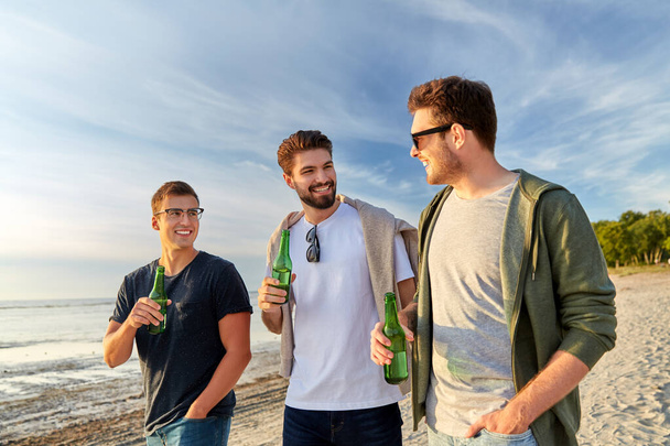 young men with non alcoholic beer walking on beach - Foto, Bild