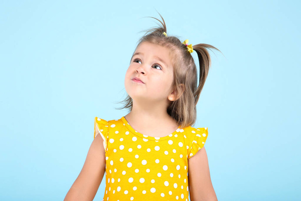 Cute little girl in yellow dress on blue background - Foto, Imagem
