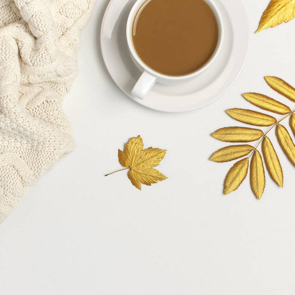 Biały kubek z kawą, złote jesienne liście, jasnobrązowa krata na jasnym tle widok z góry płaski leżał. Kompozycja z filiżanką kawy rano, gorący napój jesienny Jesienne tło Przytulne śniadanie - Zdjęcie, obraz
