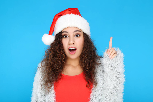 Beautiful american woman in santa hat showing finger up on blue background - Фото, изображение