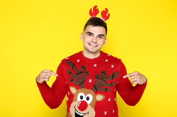 Beautiful man wearing red christmas sweater and horns on yellow  - Foto, Imagem