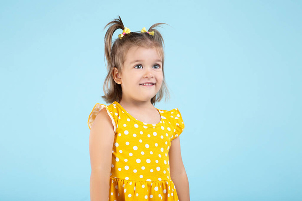 Cute little girl in yellow dress on blue background - Фото, зображення