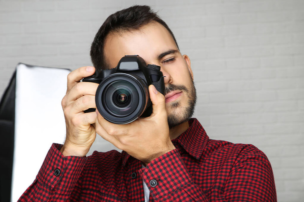 Fiatal fotós fényképezőgéppel és stúdiófelszereléssel szürke háton - Fotó, kép