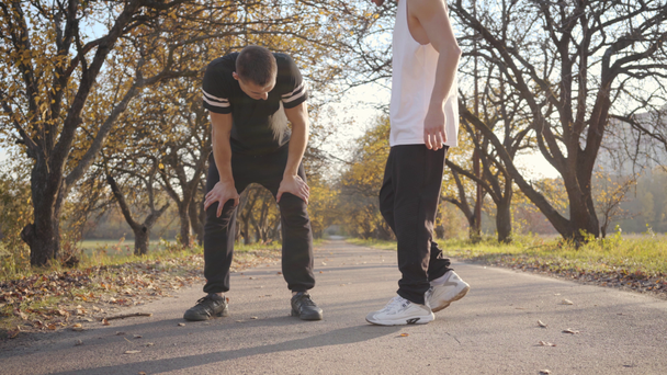 Sportliche kaukasische Jungs laufen im Herbstpark. Der erwachsene Sportler stoppte wegen Schmerzen im Knie und sein Freund kam zu Hilfe. Konzept eines gesunden Lebensstils. - Filmmaterial, Video