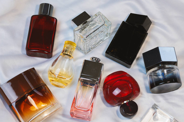 Kleurrijke mode trendy flesjes parfum toiletwater geuren liggen op een zilvergrijs laken op het bed, bovenaanzicht. Vrouwelijke en mannelijke geuren  - Foto, afbeelding
