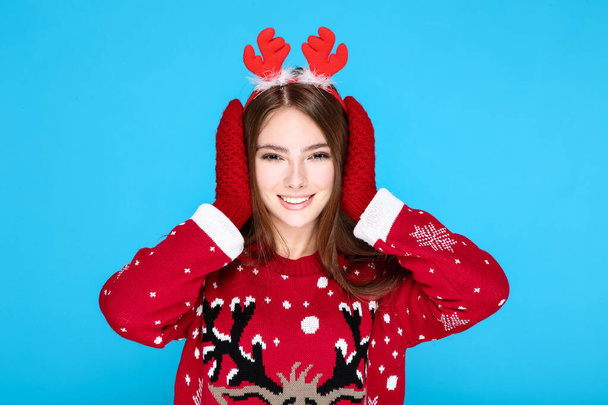 Beautiful woman in christmas sweater, gloves and red horns on blue background - Photo, image