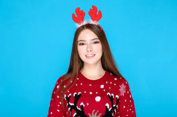 Beautiful woman in christmas sweater and red horns on blue background - Foto, immagini