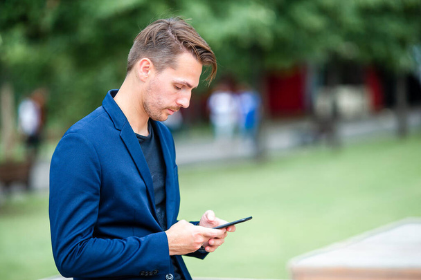 Člověk čte textové zprávy na mobilním telefonu na procházce v parku - Fotografie, Obrázek