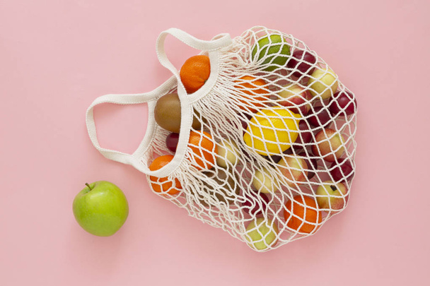Cotton mesh shopping bag with fruit on pink background. Zero waste concept. Caring for the environment and the rejection of plastic.  - 写真・画像