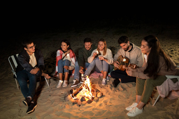 friends roasting marshmallow on camp fire on beach - Photo, image
