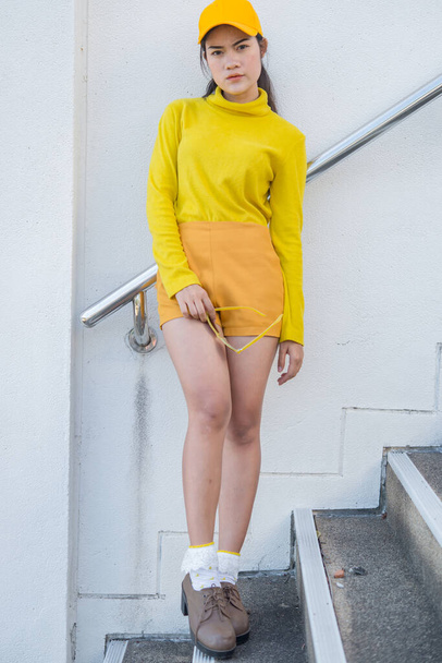 Portrait of beautiful asian woman in yellow cloths,Hipsters girl wear yellow hat on stair for take a picture,Thailand people - Foto, Imagen