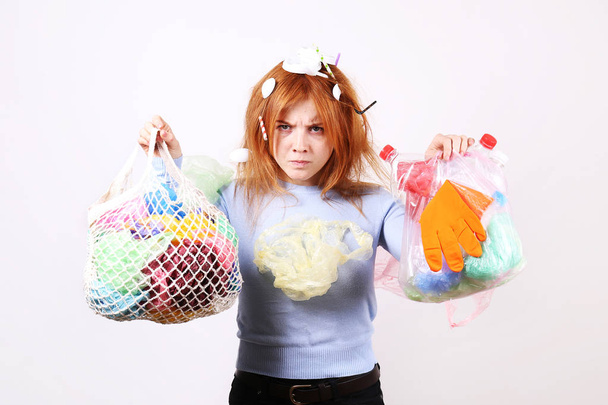 Emotional redhead woman looking stressed, covered with eco harmful plastic garbage, bags and straws of different color. Zero waste concept. Sad female frowning, angry about littering. - Foto, Bild