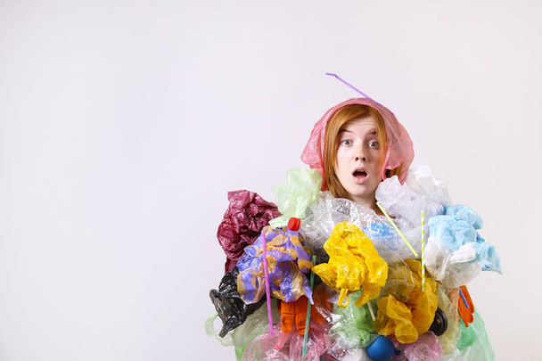 Emotional redhead woman looking stressed, covered with eco harmful plastic garbage, bags and straws of different color. Zero waste concept. Sad female frowning, angry about littering. - Foto, imagen