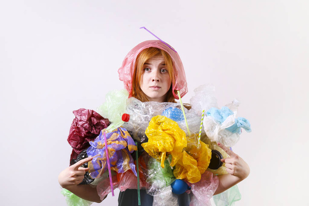 Emotional redhead woman looking stressed, covered with eco harmful plastic garbage, bags and straws of different color. Zero waste concept. Sad female frowning, angry about littering. - Foto, Imagem