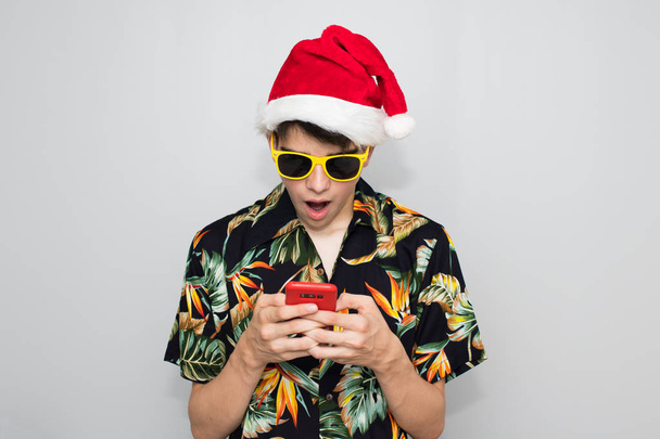 joven adolescente con camisa tropical y sombrero de Navidad en el fondo y móvil
 - Foto, imagen