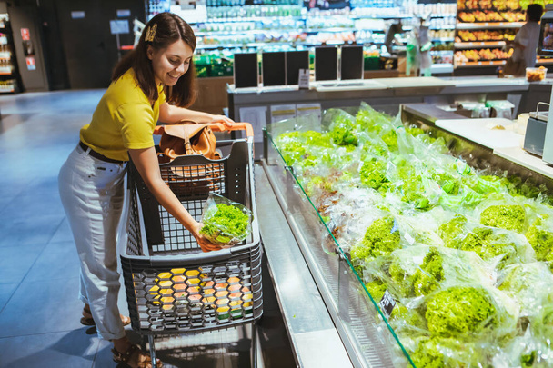 woman taking salad from grocery shopping store shelf - Foto, afbeelding