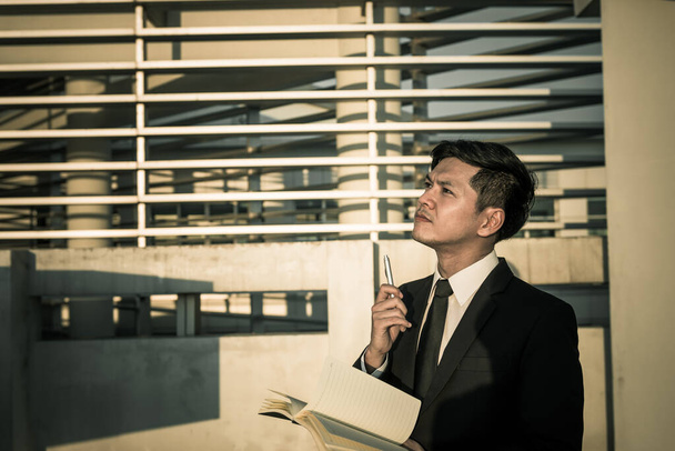 asiático hombre de negocios estrés con un libro en el edificio, él pensando algo acerca del trabajo
 - Foto, Imagen