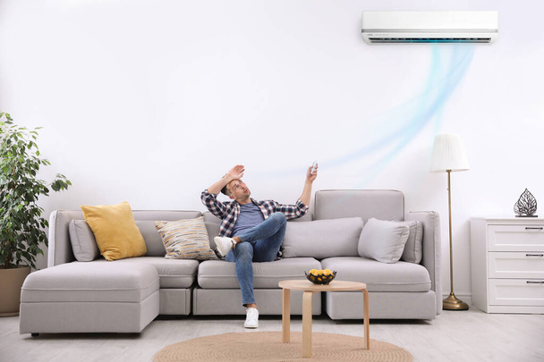 Young man switching on air conditioner with remote control at home - Foto, Imagen