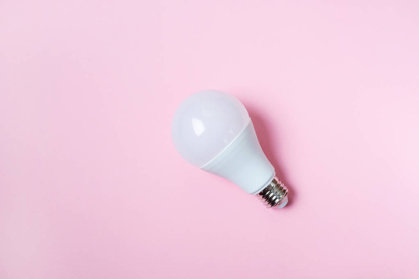 LED light bulb lies on a pastel pink background. Energy saving concept. Minimalism, top view, flat lay, place for text. - Photo, Image