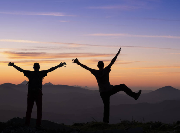 escursionisti retroilluminati in gesto celebrativo. Turista alto sulla cima di una montagna al tramonto guardando verso il paesaggio
. - Foto, immagini