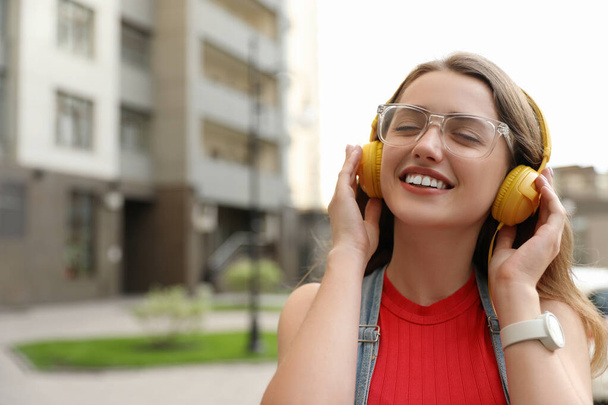 Beautiful young woman listening to music with headphones on sunny day outdoors, space for text - Photo, Image