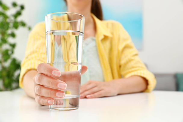 Beyaz masada bir bardak su tutan bir kadın, mesaj için yeri olan bir kadın. Tazeleyici içecek. - Fotoğraf, Görsel