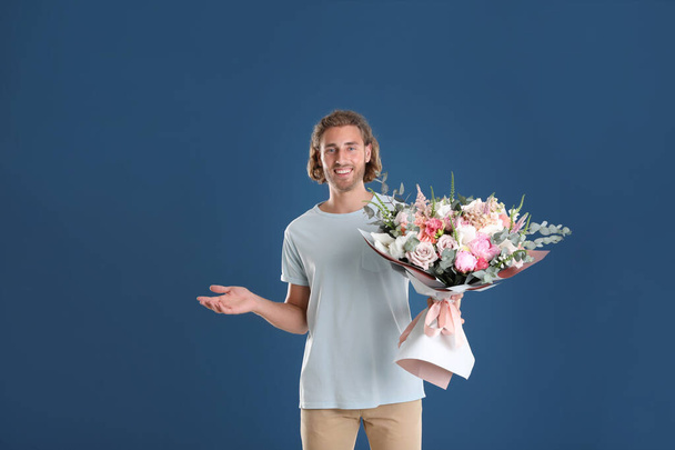 Young handsome man with beautiful flower bouquet on blue background - Fotografie, Obrázek