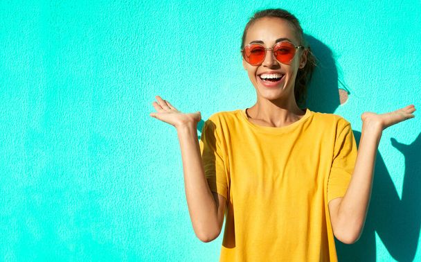 close-up portrait of fashionable smiling young woman in trendy red eyeglasses posing posing emotionally and smiling on blue background. - Φωτογραφία, εικόνα