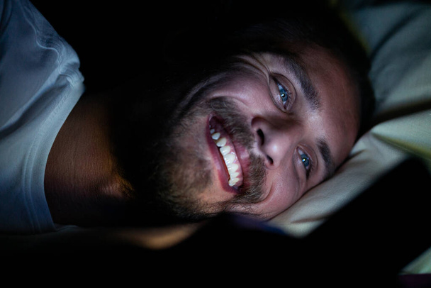 bärtige glückliche junge Mann liegt in seinem Bett und lächelt, während wa - Foto, Bild